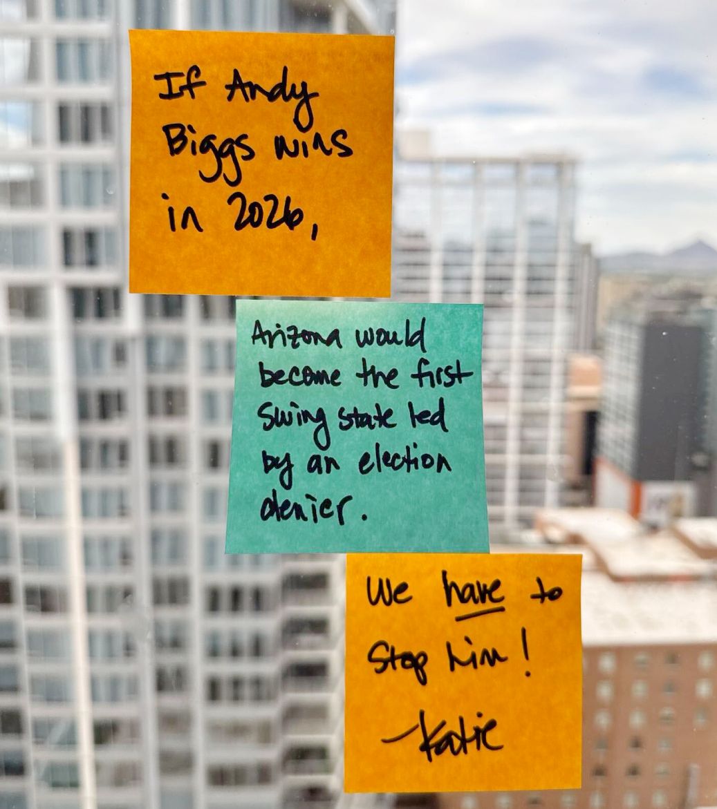 Three sticky notes, orange, blue, and orange, stuck on a window; read: 'If Andy Biggs wins in 2026, Arizona would become the first swing state led by an election denier, We have to stop him! - Katie'