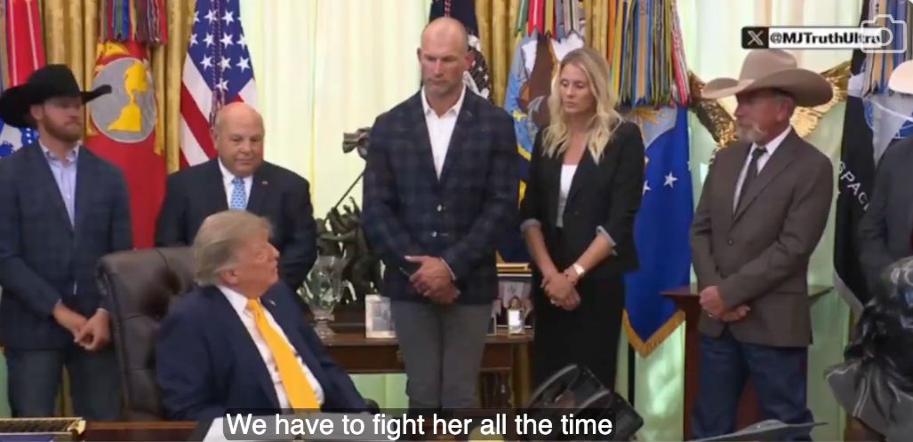 Donald Trump sits at a desk in the Oval Office while several people stand around him, including two men in cowboy hats. Subtitles at the bottom read, 'We have to fight her all the time.'